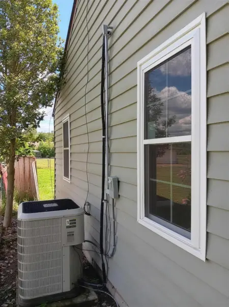 Finished window on a beige house beside an AC unit and routed electrical wiring