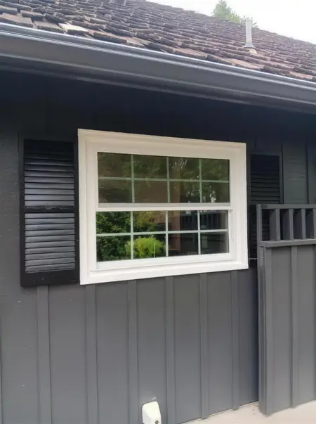 New window flanked by black shutters on a dark house