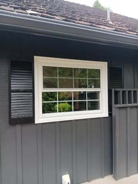 New window flanked by black shutters on a dark house