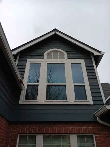 Arched transom over a three-wide window in the gable of a dark blue house above brick