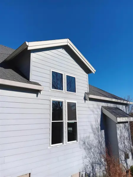 Two stacked pairs of new white double-hung windows in the gable of a light blue lap-siding house under a deep blue sky