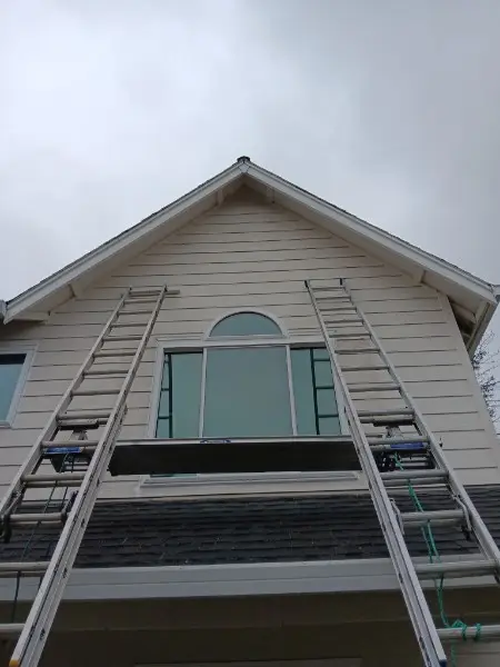 Two ladders set against a cream gable with an arched transom window mid-replacement