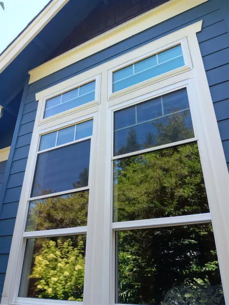 Tall white-trimmed windows with rectangular transoms on a blue-sided home