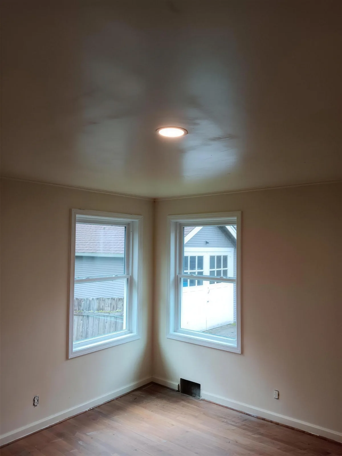 Two white-trimmed windows meeting at the corner of a room with a wood floor