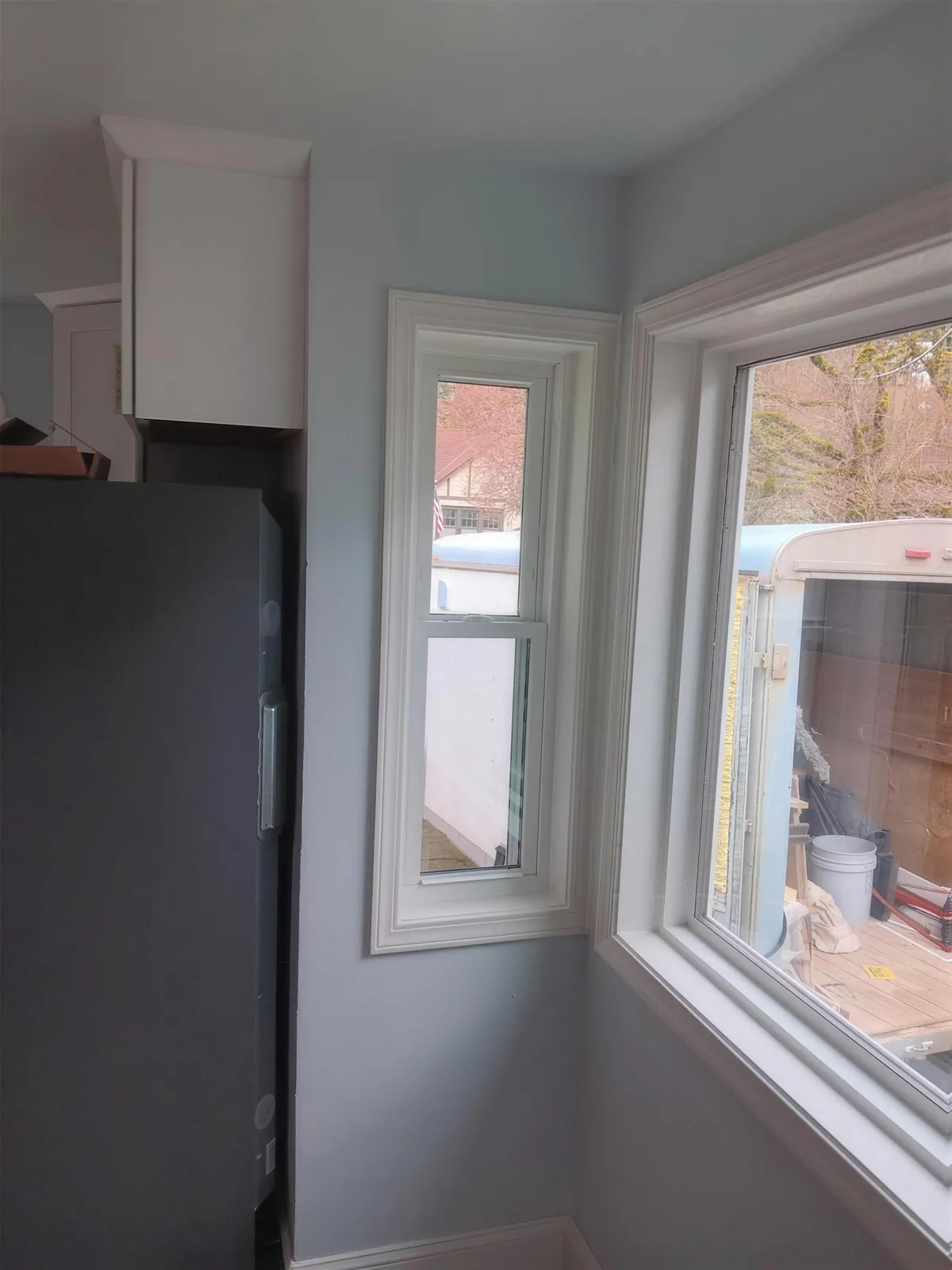 White-trimmed tall window beside a wider window in a light-colored kitchen