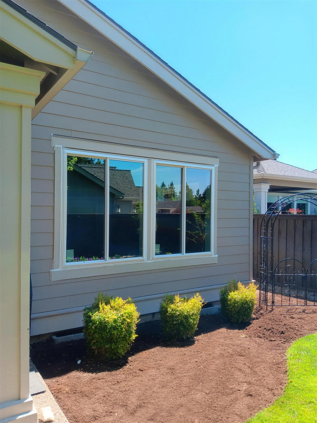 White three-panel window on a light-sided home above a landscaped garden