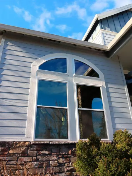 Pair of new white double-hung windows with arched transoms above, on light gray lap siding over a stone veneer base