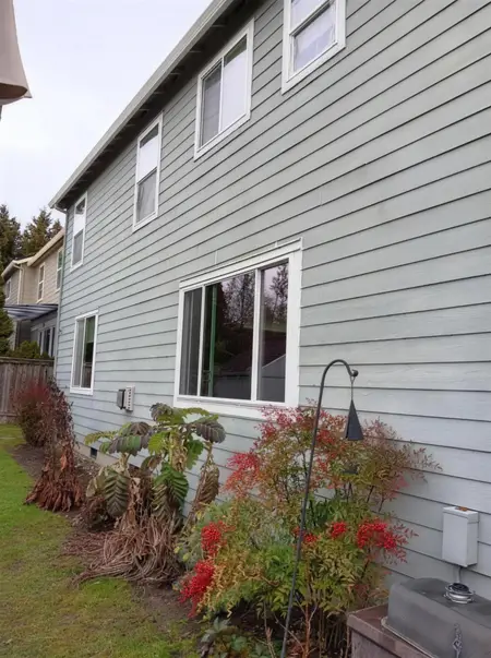 Side of a gray lap-siding house with a new white slider and upper windows