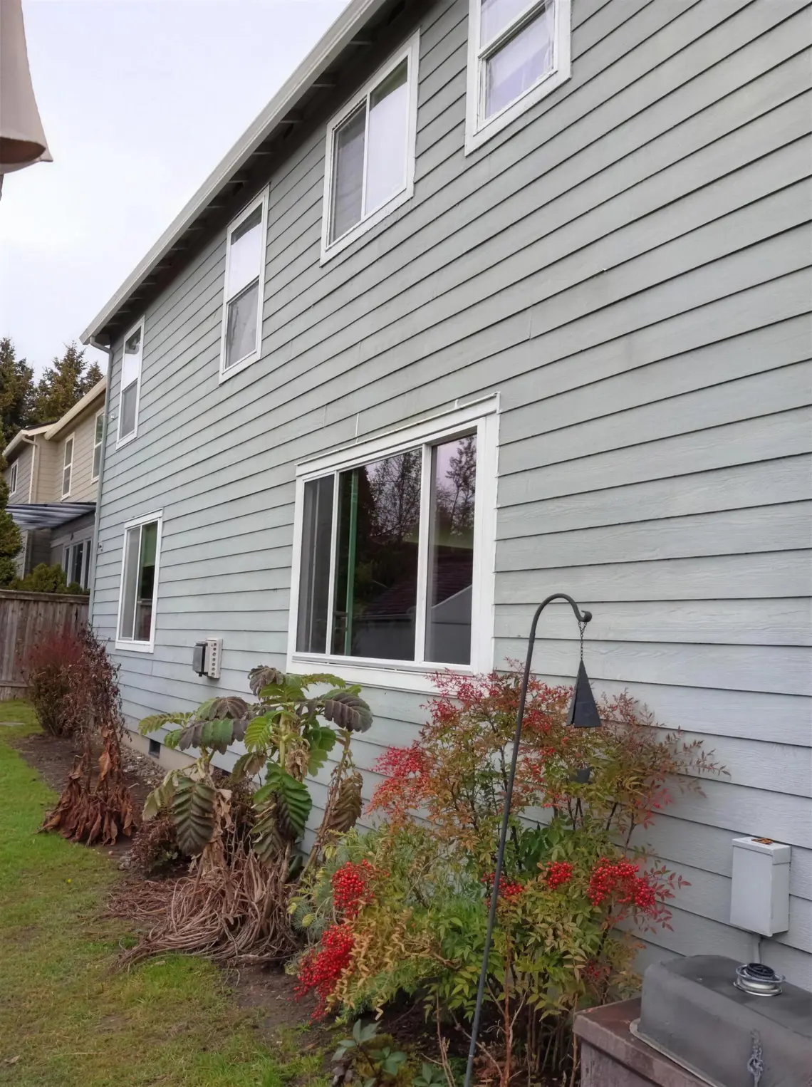 Side elevation of a gray lap-siding house with a new white slider and upper windows, showing the finished scale of a replacement project.