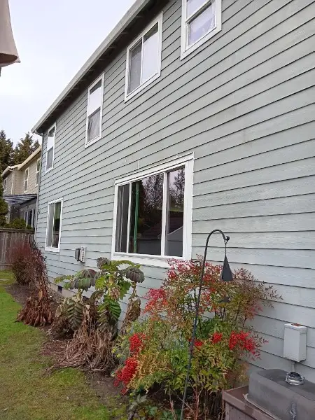 Side elevation of a gray lap-siding house with a new white slider and upper windows