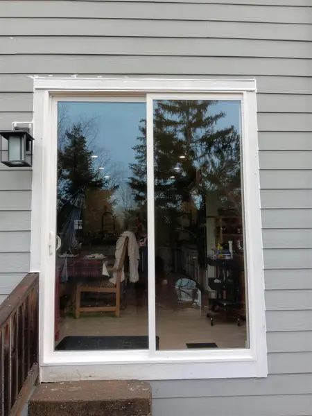 Finished two-panel white vinyl sliding glass door on a gray lap-siding house, seen from a wood deck
