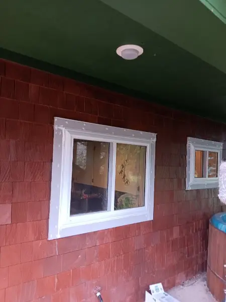 White-trimmed slider window on red cedar shingle siding under a green porch ceiling