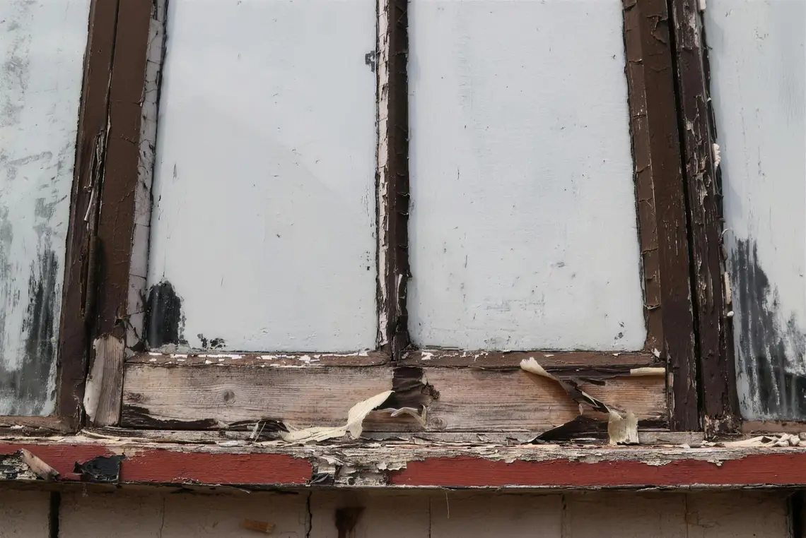 A weathered window frame with peeling paint and exposed wood, an example of the wear that signals a window is due for replacement.