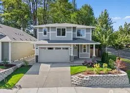 Front elevation of a light blue-gray two-story house with new windows, garage, and landscaped retaining walls