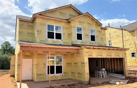 Two-story new construction wrapped in weather-resistant barrier with windows set and an open garage bay, ready for siding