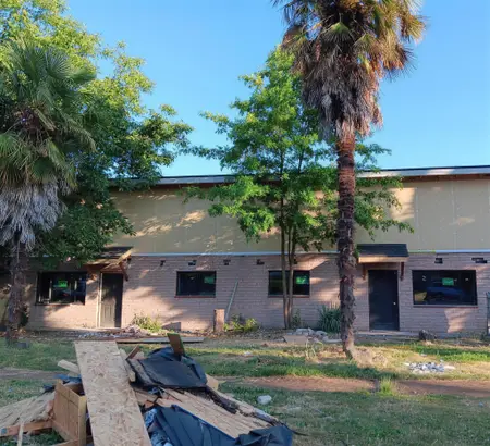Single-story brick building with new black-framed windows and tan panels covering the upper wall, with a pile of removed material in the foreground