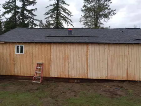 The same building with vertical wood siding panels covering the wall, a stepladder against it and one small window